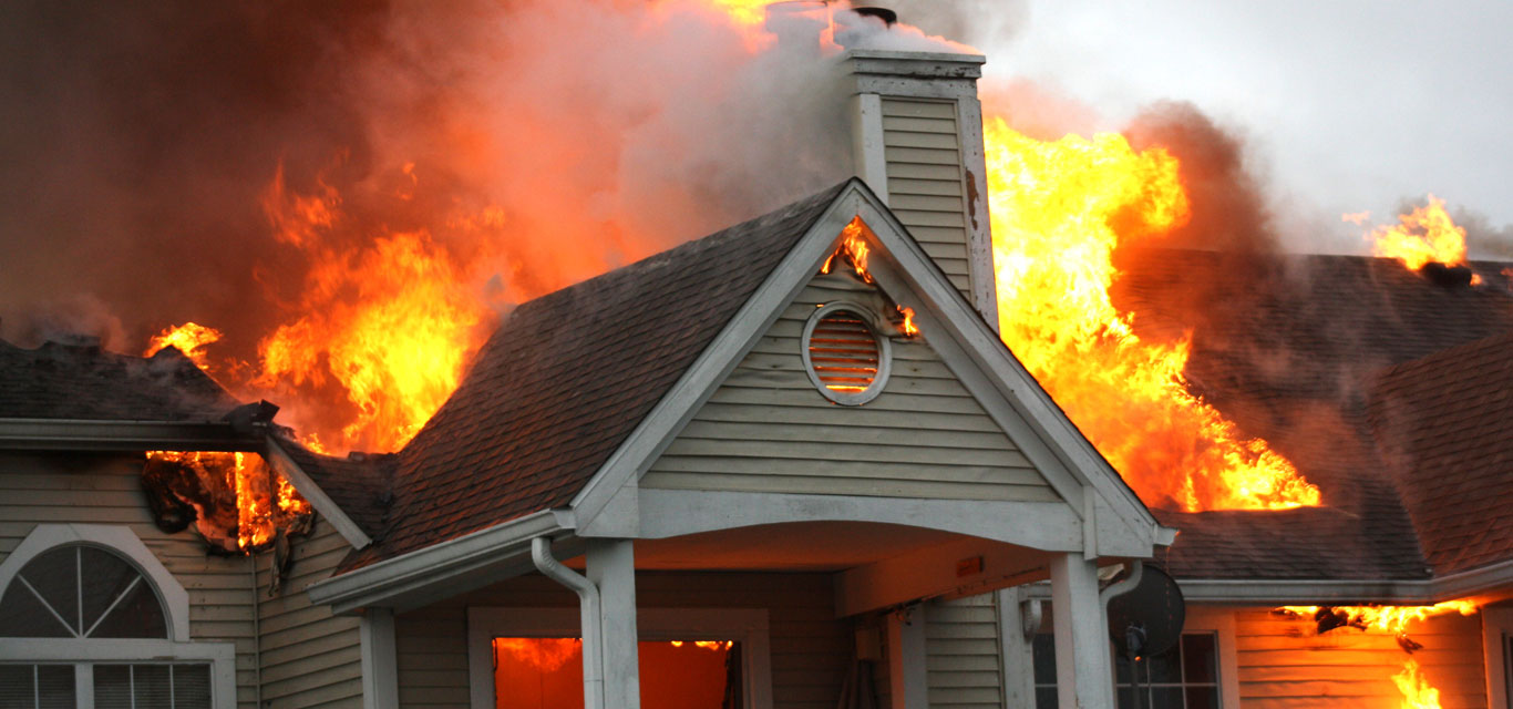 A house engulfed in intense flames and thick smoke. The fire consumes the roof, creating a dramatic and urgent scene of destruction and danger.